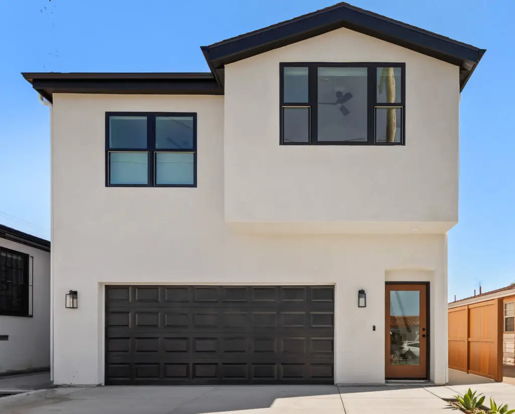 Modern two-story house with white facade, dark trim, large windows, and double garage.